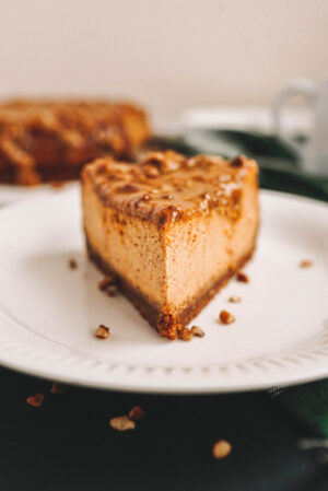 A slice of pumpkin cheesecake topped with maple pecan sauce on white plate on a black background