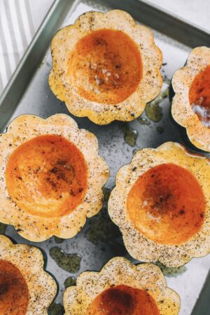 halved acorn squash topped with salt and pepper on gold baking sheet